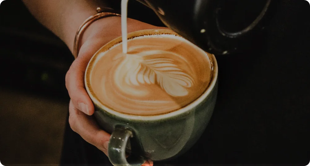 Person making latte art in a green coffee cup