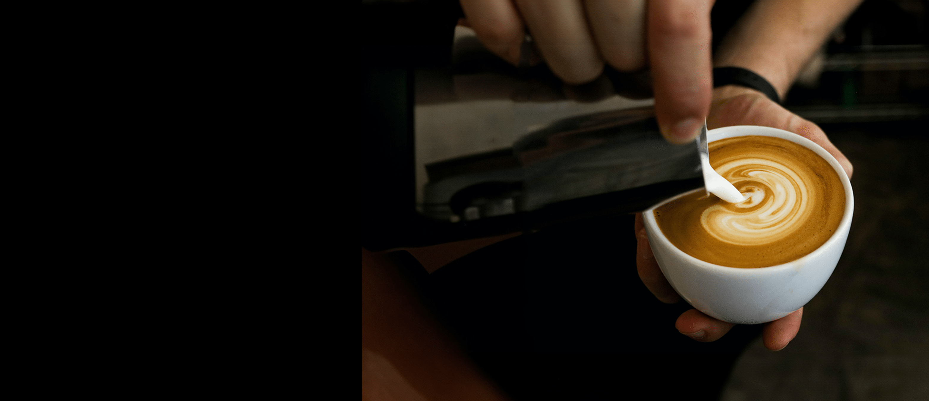 A barista preparing a coffee drink, pouring milk into a pattern in a white porcelain cup