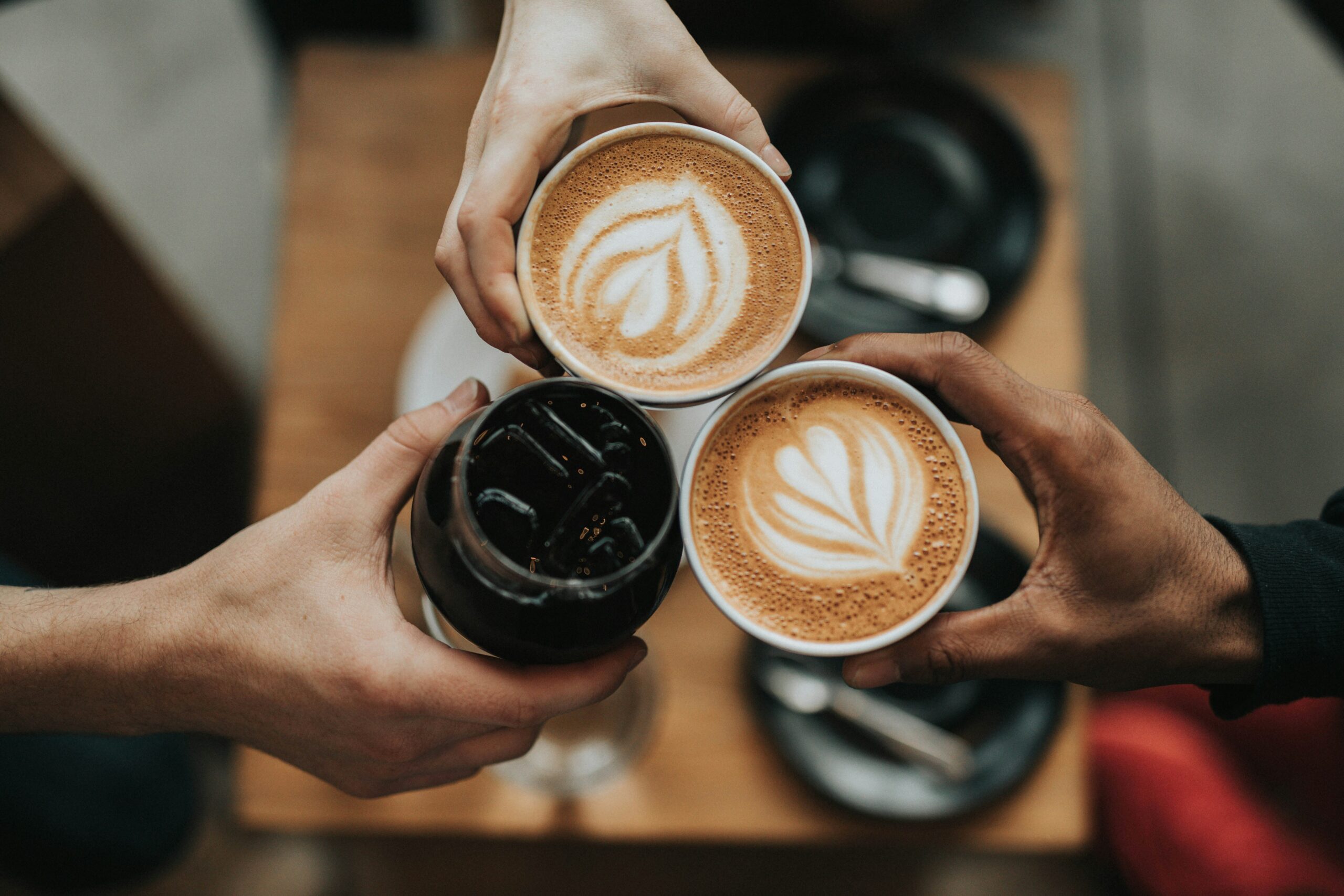 Three people holding a coffee and cold drink together