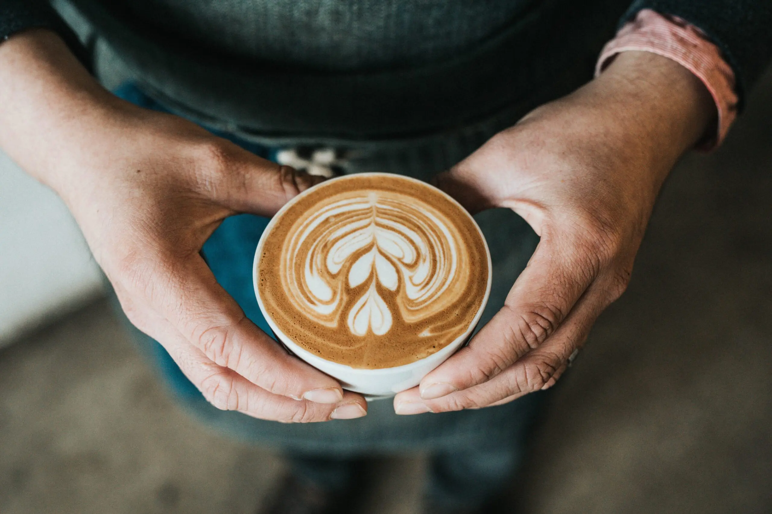 A person holding a cup of coffee with latte art in the shape of a leaf