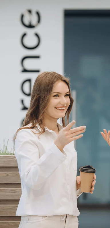 A young brunette white woman smiling with a takeaway coffee cup