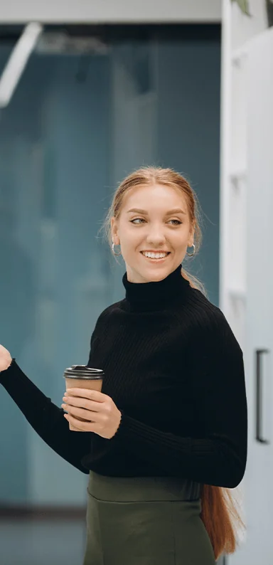 A young blonde white woman smiling with a takeaway coffee cup