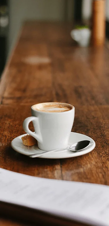 An espresso cup filled with coffee and a biscuit on a saucer on a wooden table