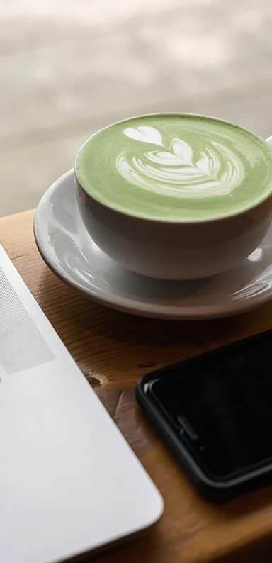 A matcha latte next to a laptop and phone