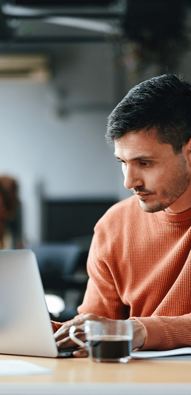 A serious Caucasian entrepreneur typing on his laptop while sitting at the office desk.