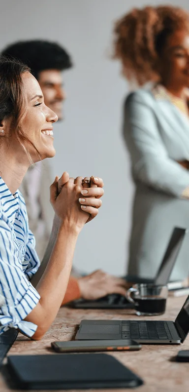 A white woman smiling in a meeting with her hands clasped together