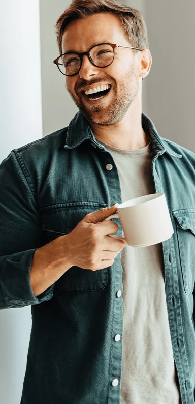 A young white man smiling with a cup of coffee