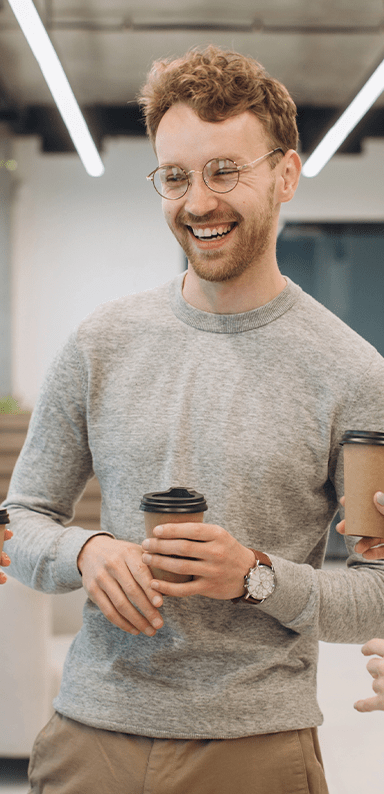 A young white man smiling with a takeaway coffee cup