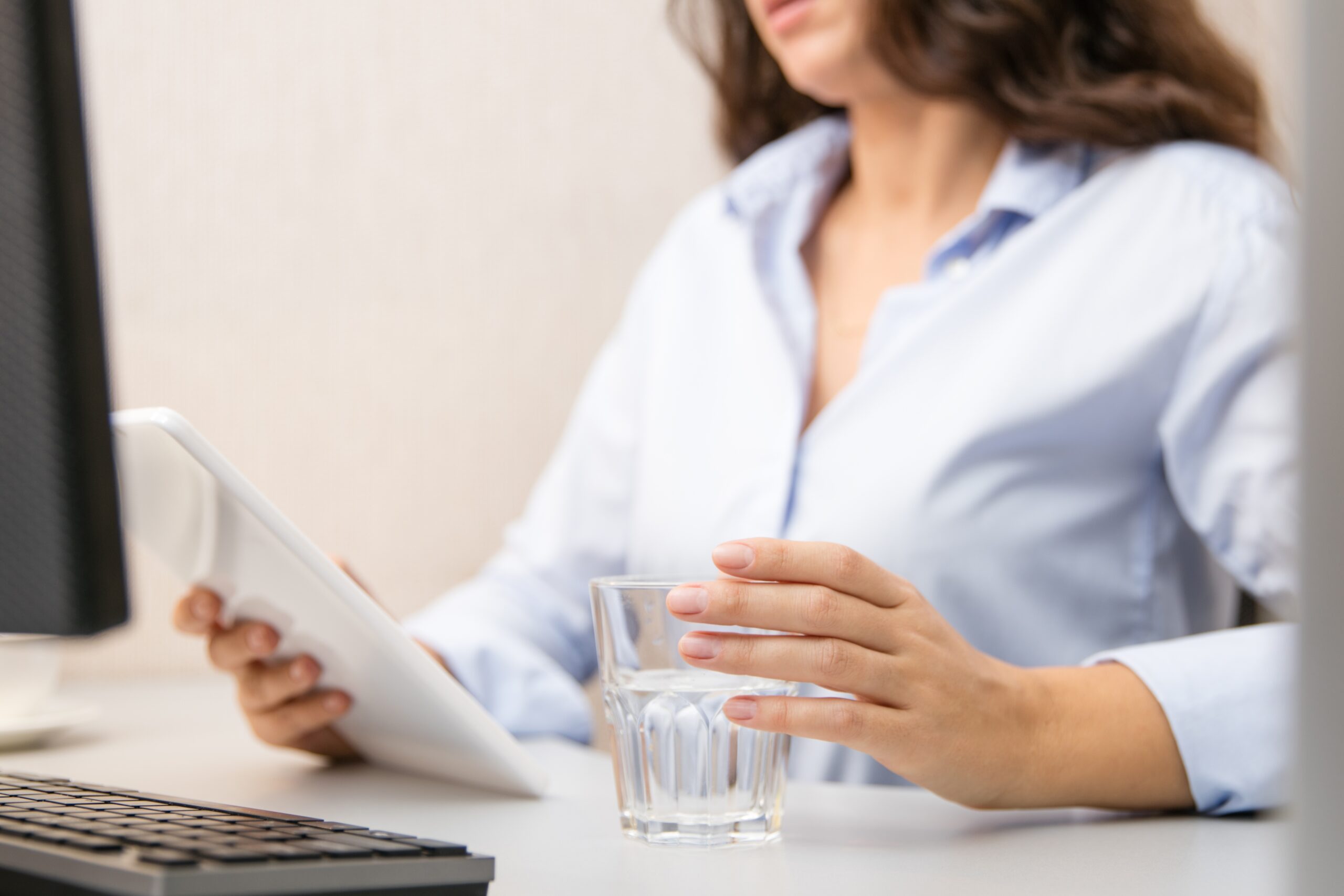 A woman holding a glass of water while looking at an ipad