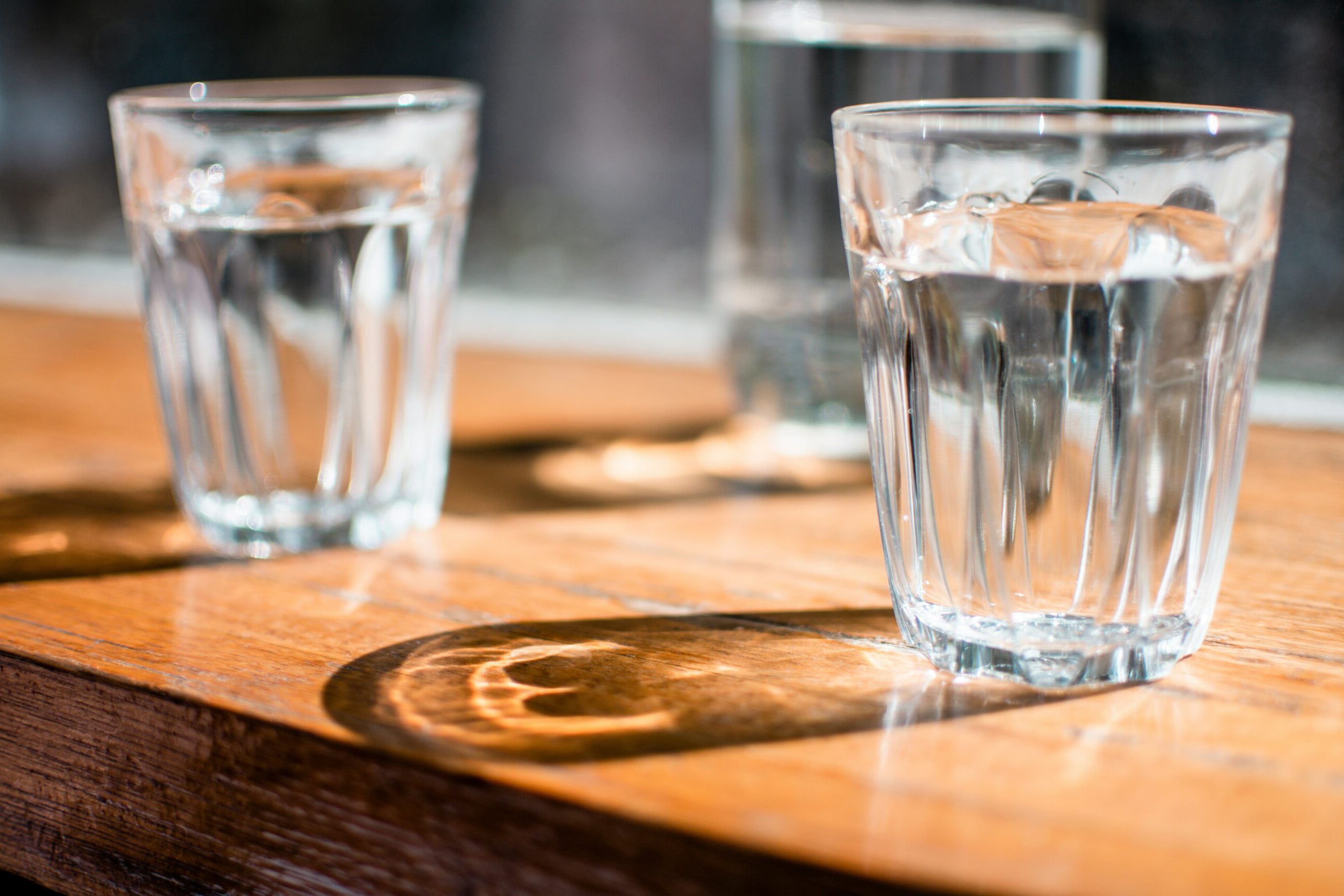 Three glasses of water with their shadows reflecting on a wooden surface