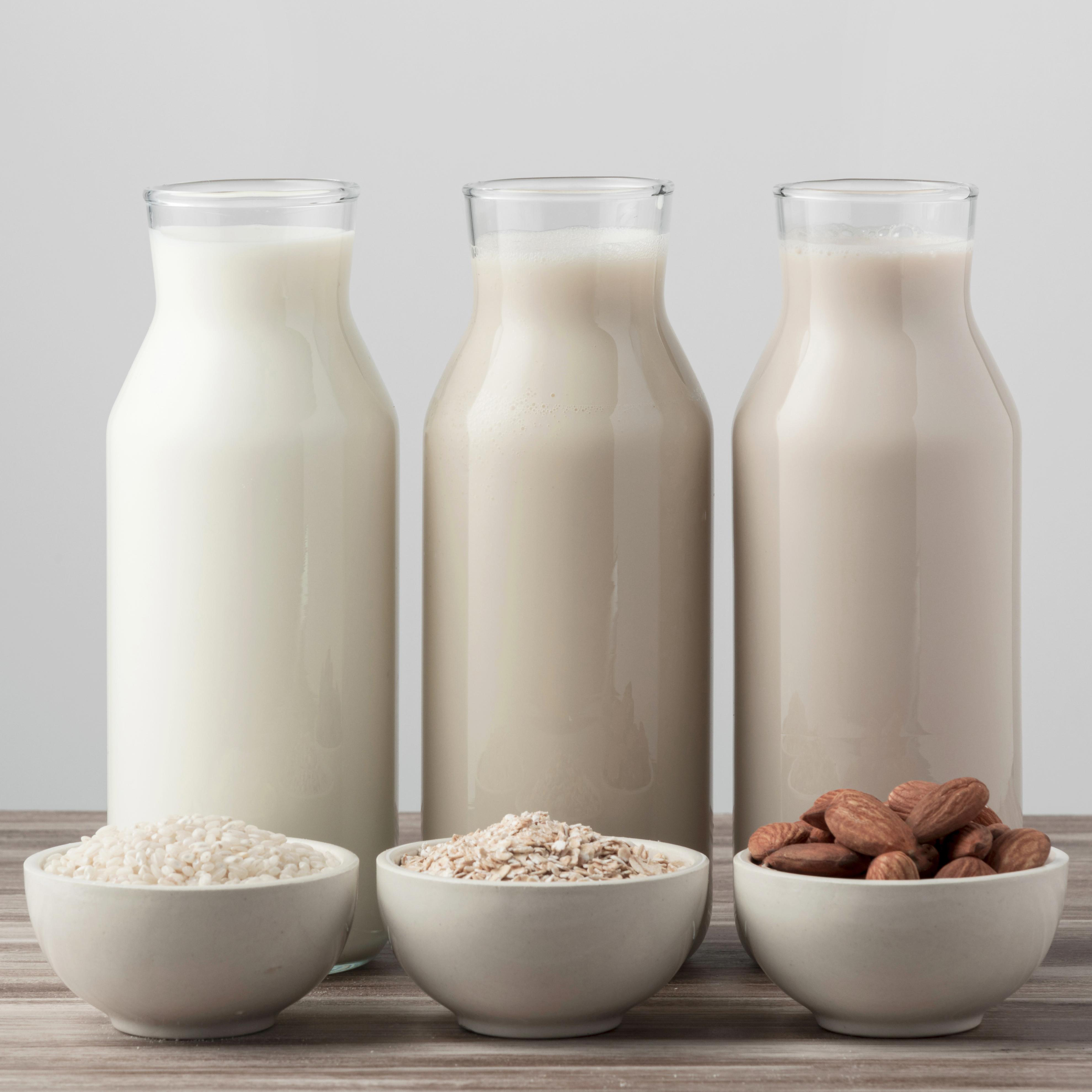 Dairy milk alternatives in a jug and in a bowl including soya, oat and almond nuts