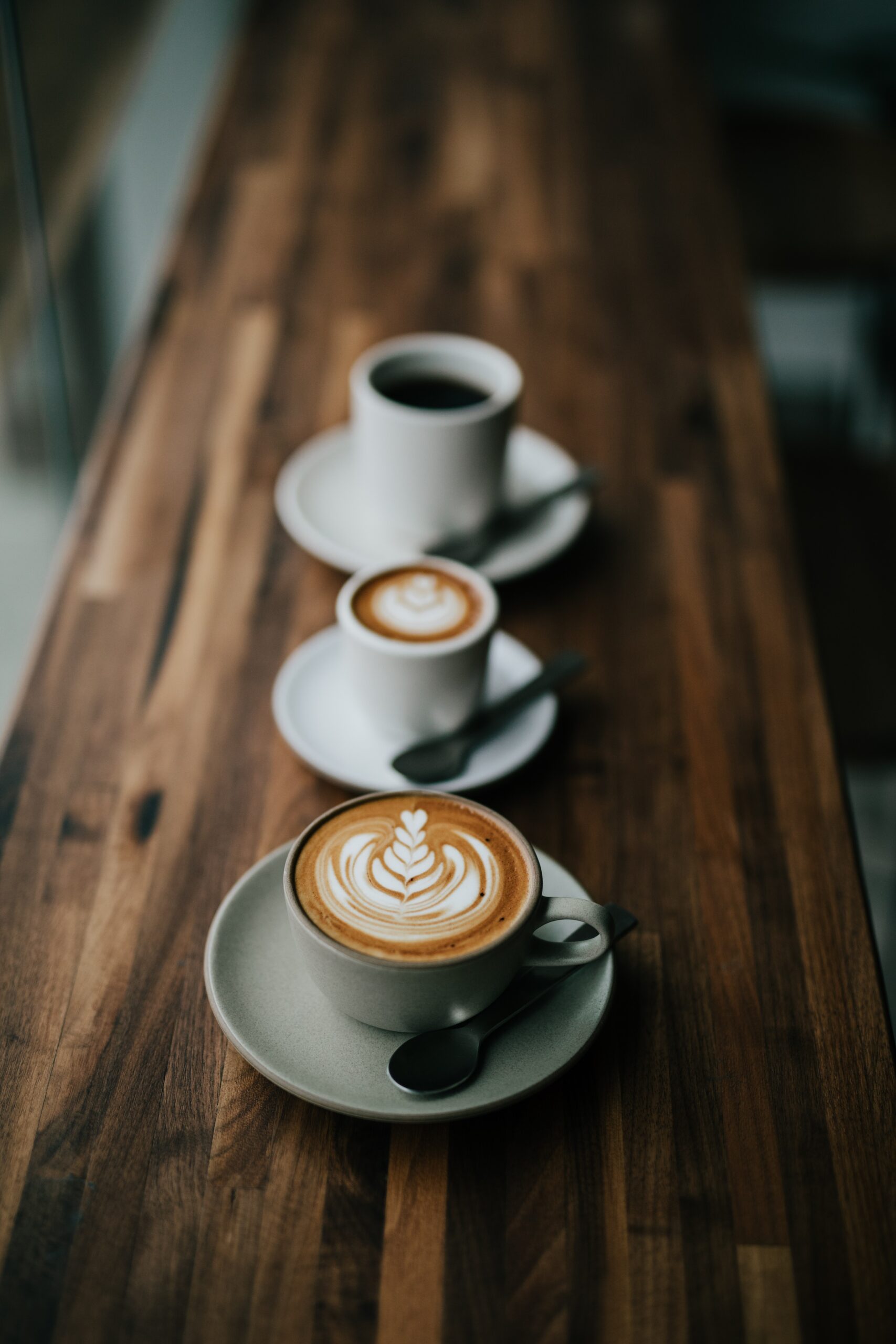 A row of three coffee cups with latte art on a dark wooden table