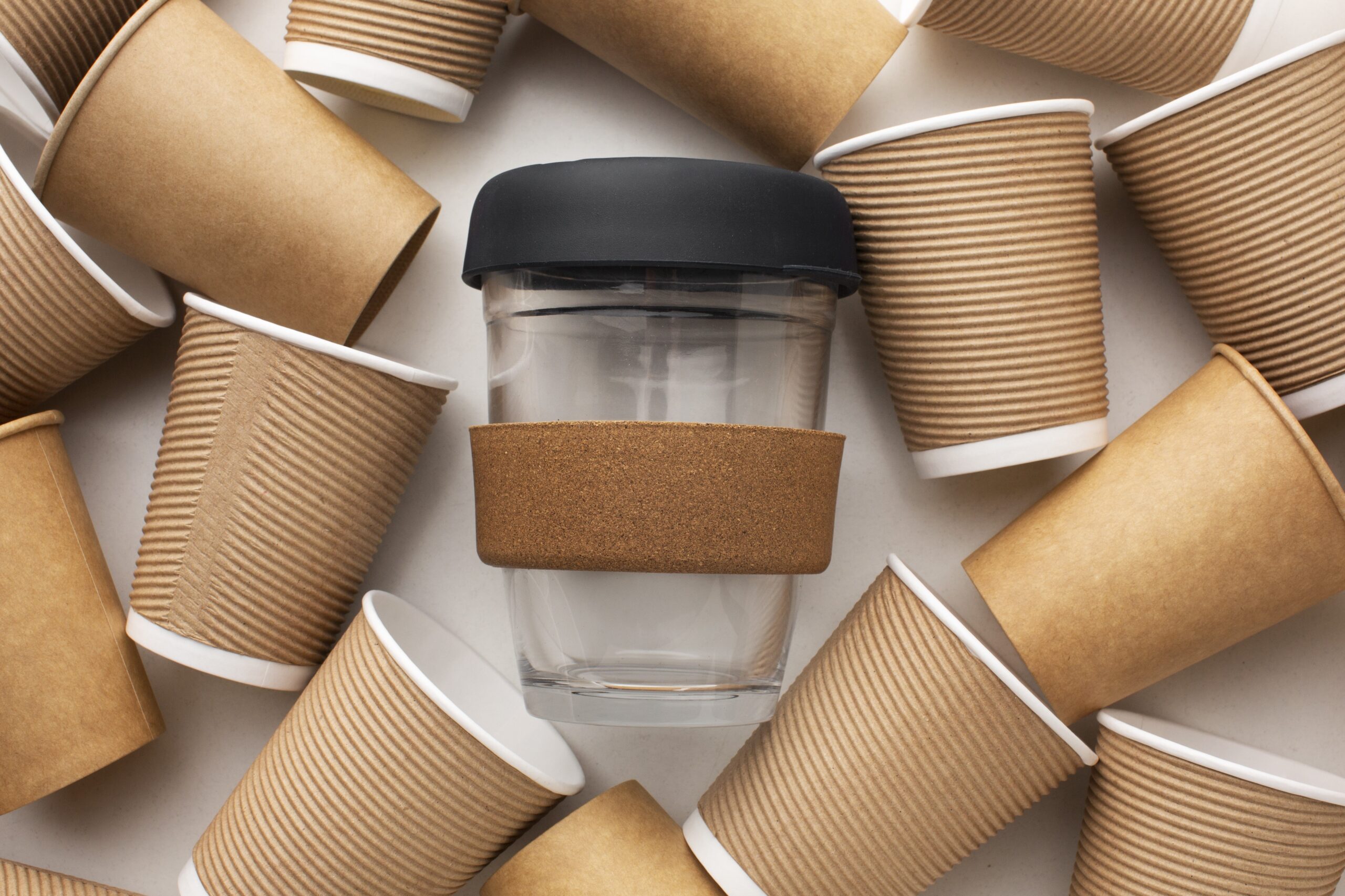 A reusable glass takeaway cup surrounded by recyclable paper cups