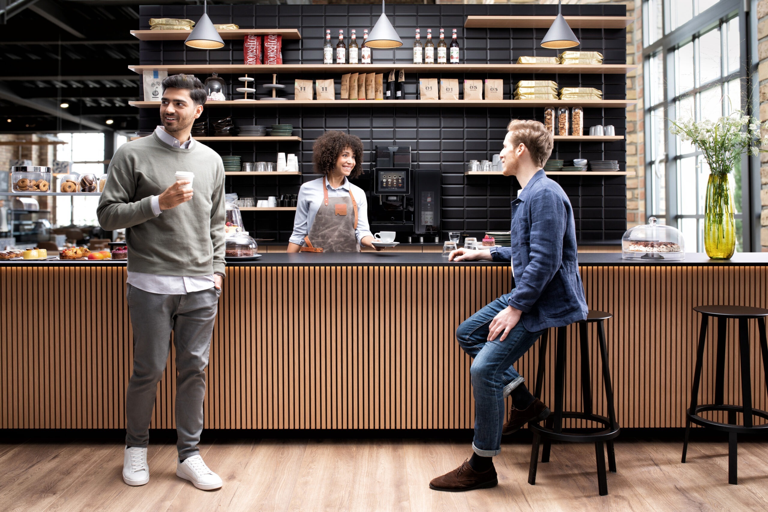 A coffee shop scene with a Franke A800 commercial coffee machine featuring two men and a female barista serving them a cup of coffee