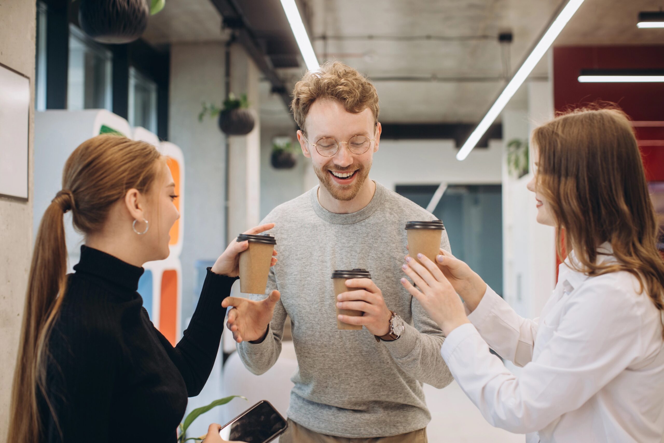 A man and two women in an office passing one another a recyclable takeaway cup