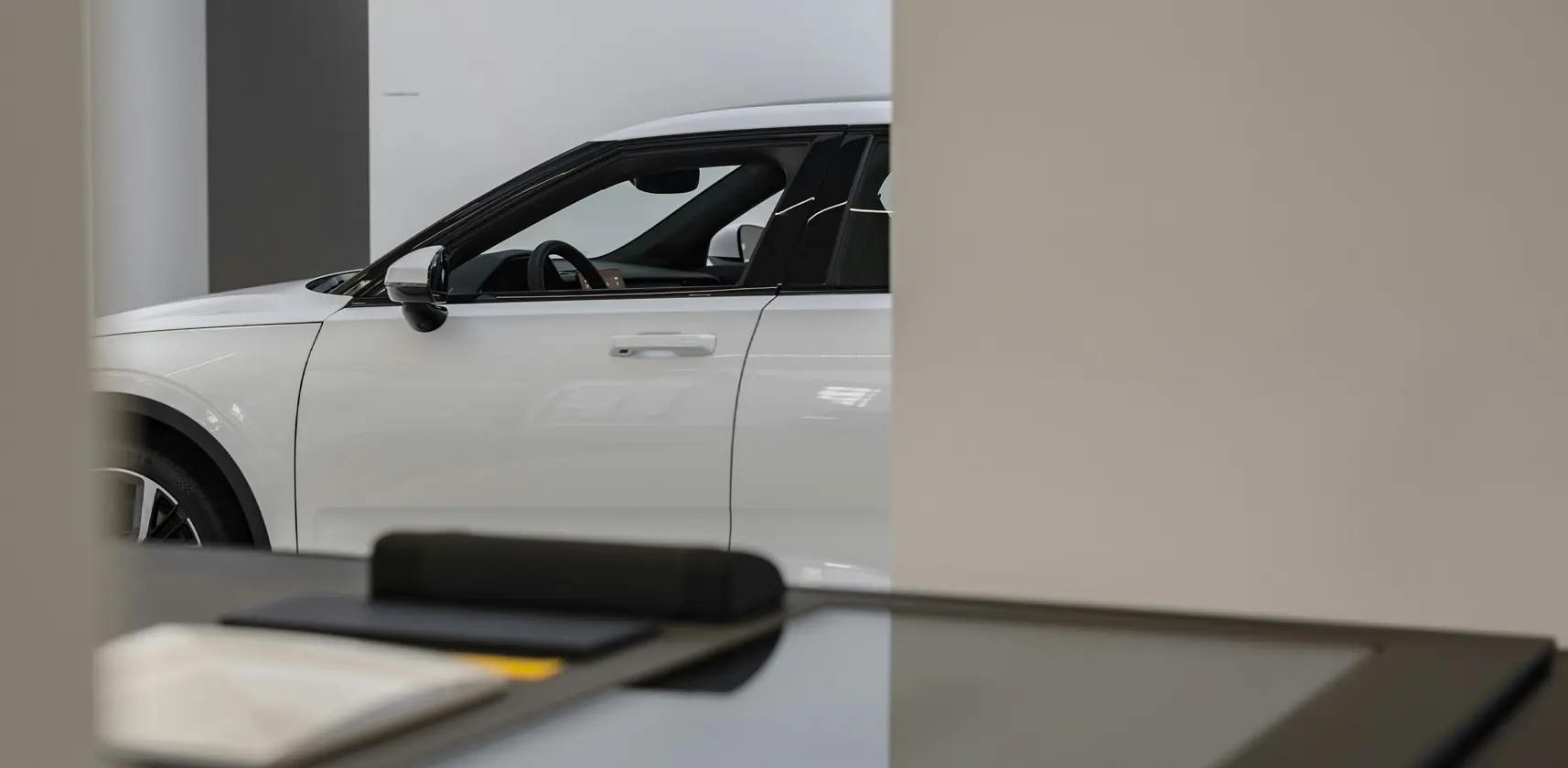 A white car in an automotive car showroom peeking out from a wall