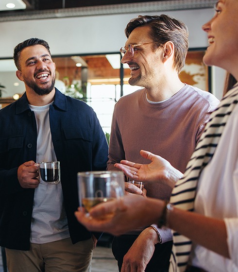 Business people laughing together during a coffee break at work. Group of young professionals standing together in an office.