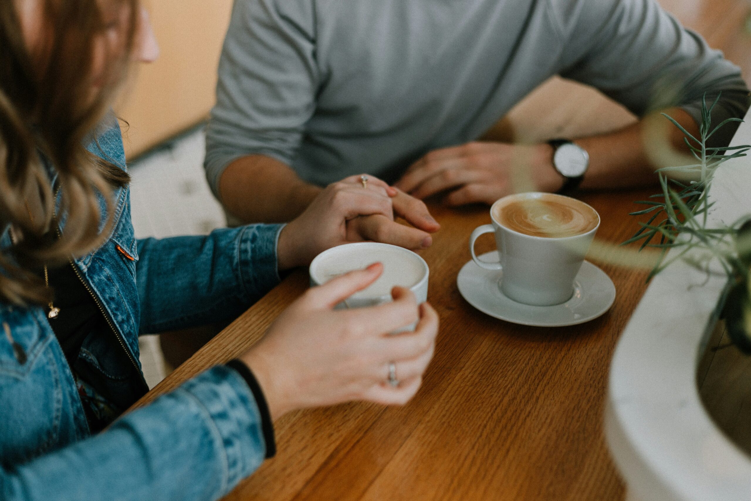 A couple sat at a table holding hands next to two cups of coffee